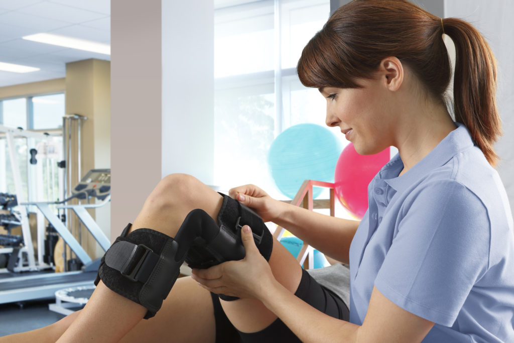 Female Physical Therapist Adjusting Knee Brace On Female Patient